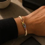 Weißes Kordelarmband mit einem mehrfarbigen geometrischen Edelstein als Mittelstück am Handgelenk.