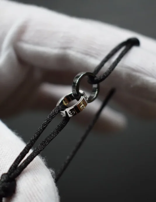 White gold black cord bracelet with 18k gold ring centerpiece held in gloved hands
