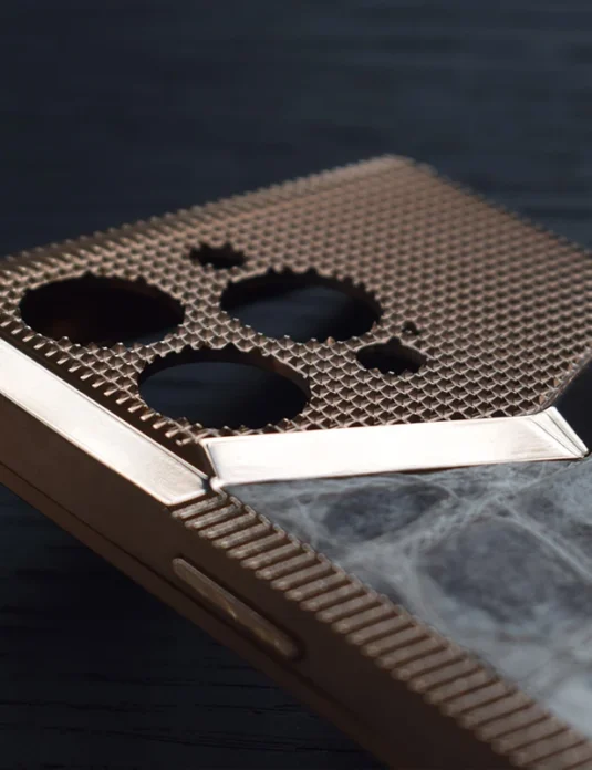 Rose gold titanium iphone case with honeycomb mesh pattern and marble back panel on dark surface