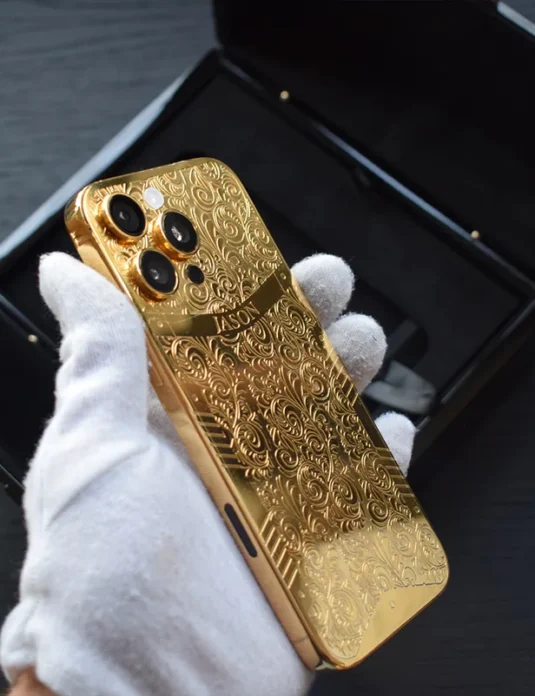 Gold engraved iPhone 16 Pro Max with ornate floral pattern held in white gloves