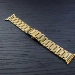 سوار ساعة أبل من الذهب عيار 24 قيراطًا بوصلات مستطيلة مصقولة، معروض على سطح خشبي داكن