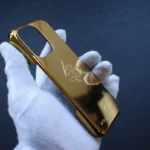 Paraurti per custodia iPhone in oro 24k tenuto in mani guantate di bianco che mostrano finitura a specchio e stemma a foglia