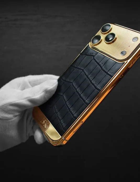 Gold crocodile iPhone 17 Pro Max with 24k gold plating and black crocodile leather held in white gloved hand