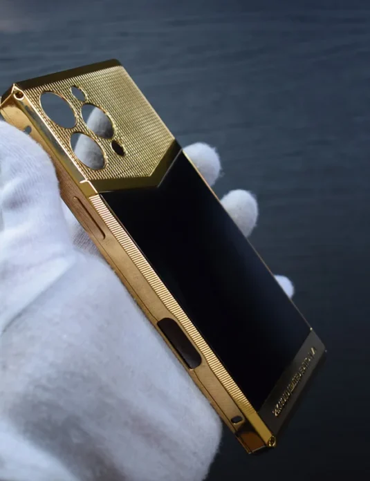 Gold iPhone case 16 Pro Max held in white gloved hand showing 24k gold plating and textured surface