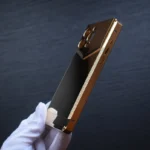 Gold metal iphone case held in white gloved hand showing luxurious metallic finish and precise construction
