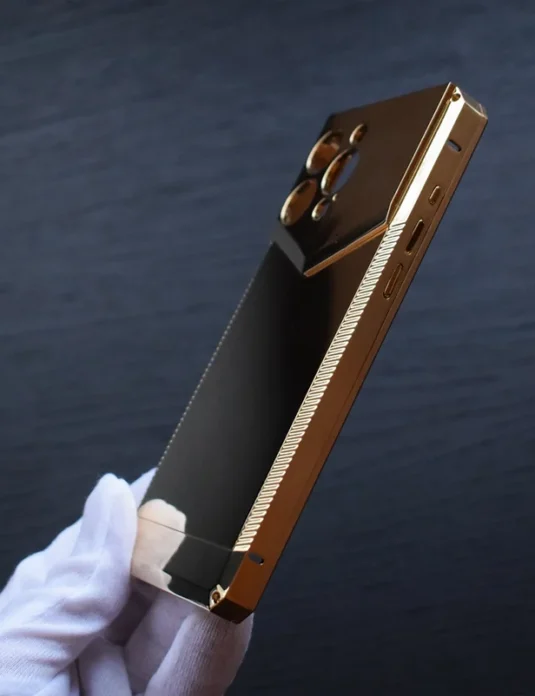 Gold metal iphone case held in white gloved hand showing luxurious metallic finish and precise construction