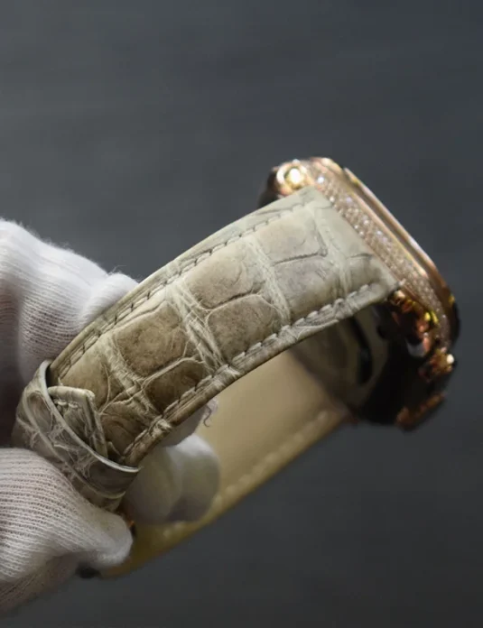 Reloj Apple Watch Ultra de oro rosa con diamante y correa de cuero de cocodrilo champagne sostenido en manos enguantadas blancas