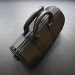 Black ostrich leather duffle bag with raised quill pattern and metal corner protectors