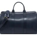 白色背景上的蓝色皮革旅行包，配有金色五金配件和肩带