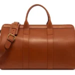 Cognac leather duffle bag with dual handles and adjustable shoulder strap showing rich brown leather construction