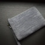 灰色磨砂皮手拿包，鳄鱼纹压花纹理，金色五金配件，置于深色木质表面上