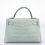 Green mint alligator handbag Kelly style with crocodile texture and gold hardware on white background