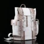 White crocodile leather backpack with brown accents and silver hardware photographed against black background