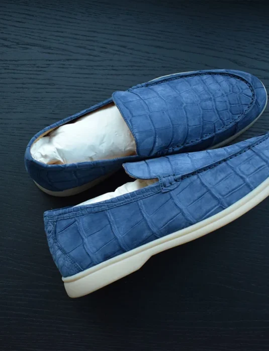 Mocassini in nubuck di coccodrillo azzurro chiaro con motivo a squame in rilievo e suole in gomma bianca su superficie di legno scuro