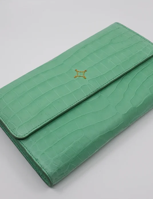 Light green crocodile clutch with envelope design showing crocodile leather texture and gold hardware