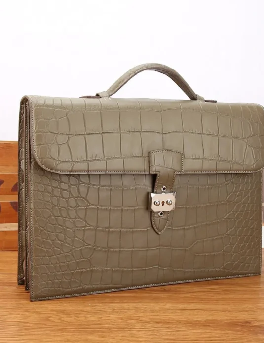 Maletín de piel de cocodrilo color caqui con acabado mate y cierre de hebilla plateada sobre superficie de madera