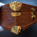 Braune Uhrenbox aus Krokodilleder mit goldfarbenen Beschlägen, die die Patina des Leders und die Innenfächer aus Wildleder zeigt