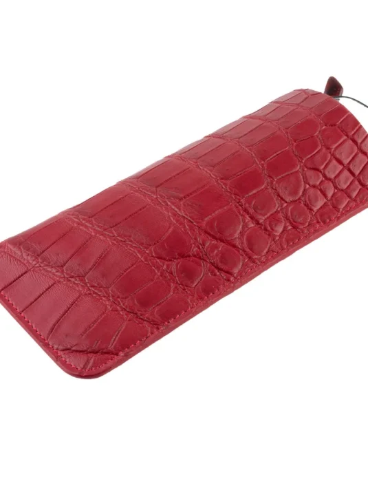 Red crocodile glasses case with textured leather surface and eyeglasses partially visible