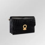 Pochette en cuir de crocodile noir avec détails dorés et dragonne assortie sur fond blanc