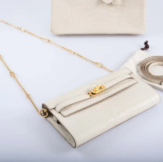 White crocodile pouch Kelly with gold chain and leather strap on marble surface