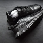 Black crocodile leather sneakers with geometric bouncing sole displayed on wooden surface