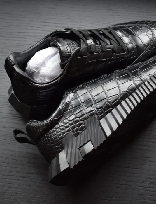 Black crocodile leather sneakers with geometric bouncing sole displayed on wooden surface