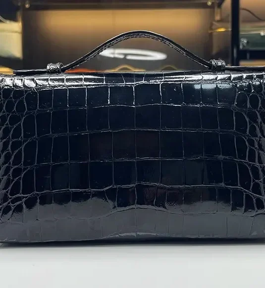 Black crocodile pouch with glossy scaled leather texture and silver hardware displayed in luxury boutique