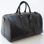 Black python duffle bag with gold hardware and dual handles showing natural scale texture
