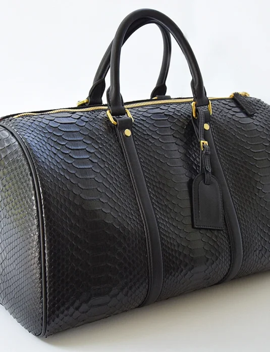 Black python duffle bag with gold hardware and dual handles showing natural scale texture