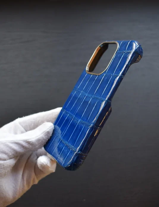 غلاف آيفون من تمساح أزرق يُمسك بيد مغطاة باللون الأبيض يُظهر نسيج القشور الزاحفة الحقيقي