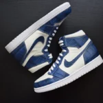 حذاء جوردن من تمساح أزرق مع ألواح جلدية مقشّرة باللون البحري وتفاصيل بيضاء على سطح خشبي داكن