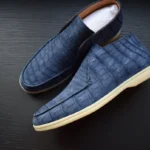 Blue crocodile leather loafers with textured nubuck finish and cream soles on dark wooden surface