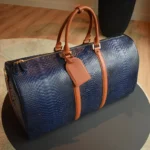 Sac de voyage en python bleu avec poignées en cuir cognac et finitions dorées sur une table noire