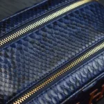Blue python leather toiletry bag with gold zippers showing scaled texture and navy coloration
