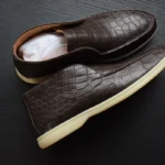 棕色鳄鱼皮乐福鞋，带鳞片图案，奶油色鞋底，置于深色木质表面