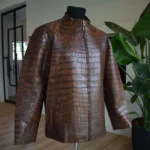 Chaqueta de piel de cocodrilo marrón exhibida en un maniquí que muestra la textura detallada de las escamas y el cierre frontal con cremallera