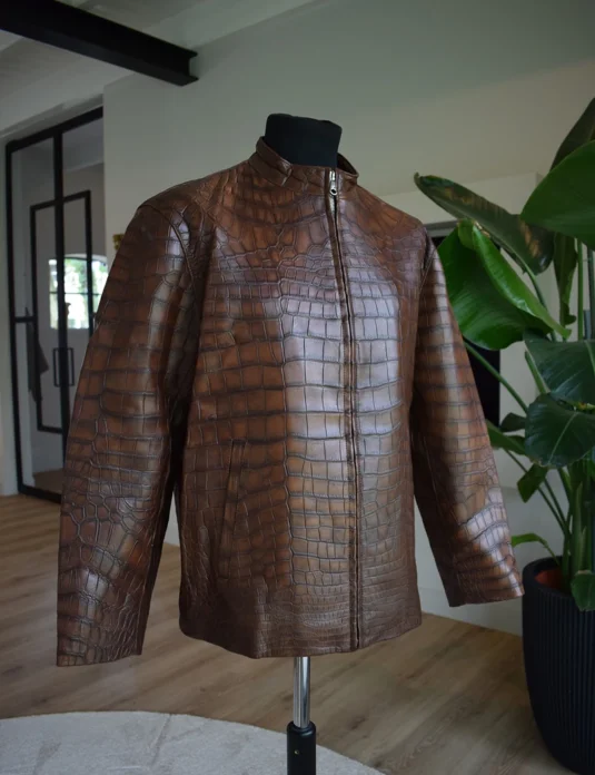 Chaqueta de piel de cocodrilo marrón exhibida en un maniquí que muestra la textura detallada de las escamas y el cierre frontal con cremallera