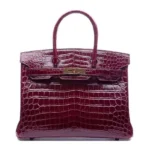 Burgundy crocodile leather handbag with Birkin design showing scaled texture and gold hardware