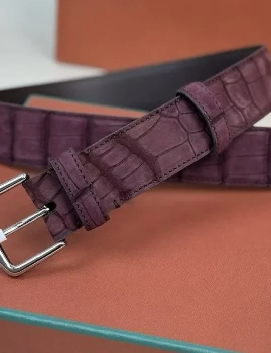 Burgundy crocodile leather belt with silver buckle displayed on orange luxury packaging