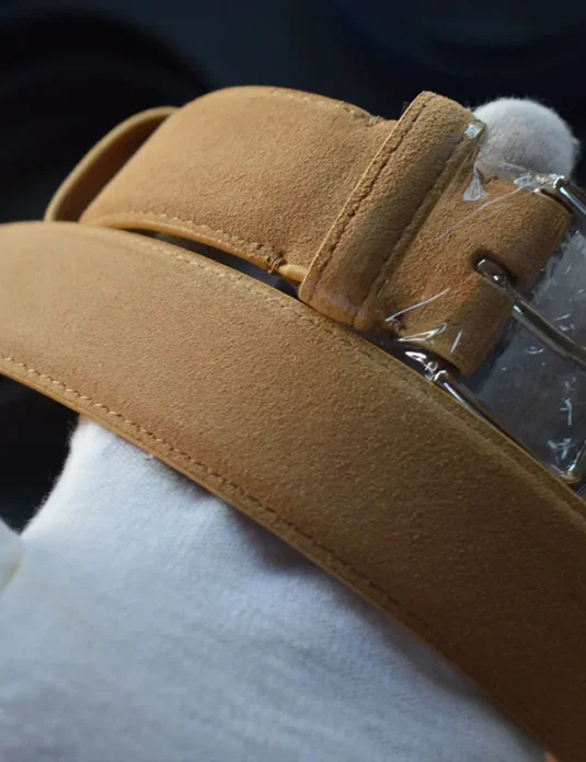 Kognak Wildledergürtel mit silberner rechteckiger Schnalle, gehalten von weißen, behandschuhten Händen