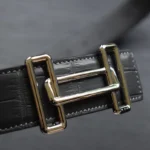 黑色鳄鱼皮腰带，配金色 H 型扣，展示独特的矩形鳞片图案