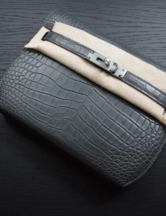 黑色鳄鱼纹凯莉Depeche包，配有银色金属配件和旋转锁闭合，展示在深色表面上