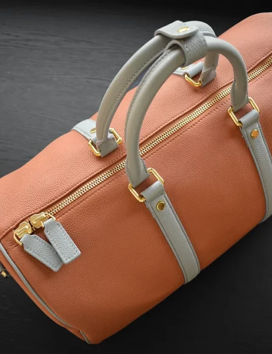 Brown togo leather duffle bag with grey handles and gold hardware on dark surface