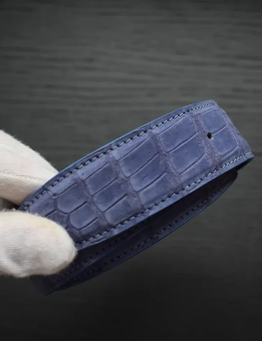 حزام من جلد تمساح أزرق داكن بلمسة نوبك تُظهر نسيج قشور مفصل وحواف مخيطة يدويًا