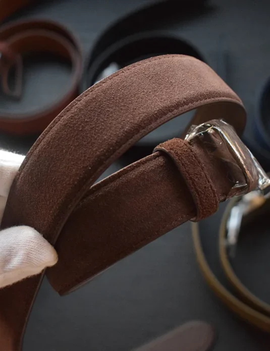 حزام من الجلد المدبوغ الأحمر الداكن مع مشبك فضي يُمسك بيده مكسوة بالقفاز يُظهر الحرفية