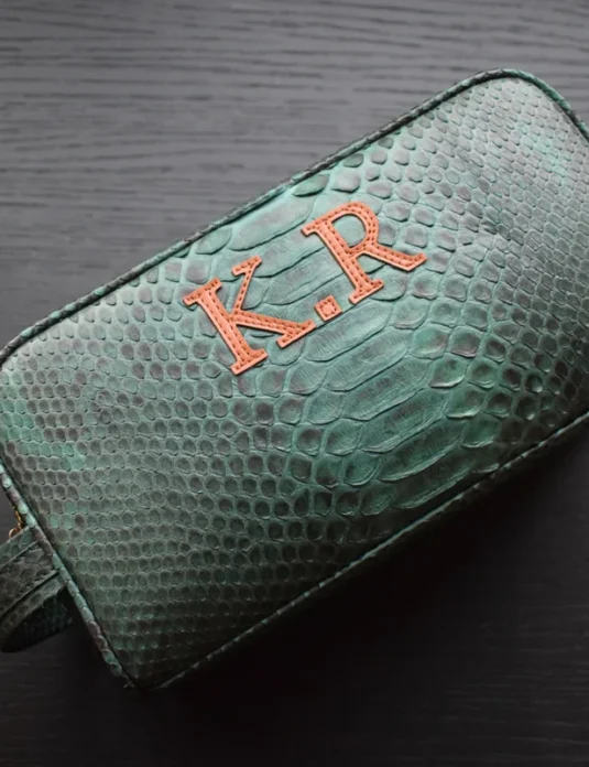 Green crocodile leather toiletry bag with coral monogram embroidery on textured exotic leather surface
