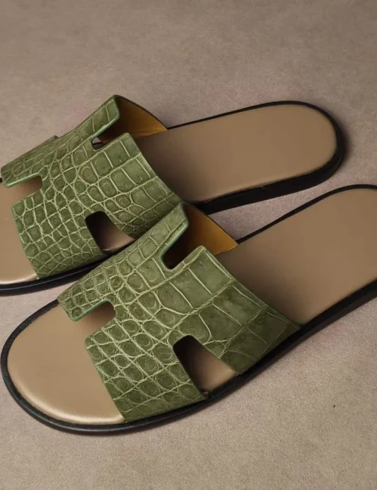 Green crocodile leather sandals with H-shaped straps and nubuck texture on beige background