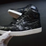 Dark blue crocodile Jordan sneakers with patina finish held in hand showing scaled leather texture