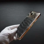 Platinum crocodile iPhone 17 Pro Max with black crocodile leather back and rose gold frame held by white gloved hands