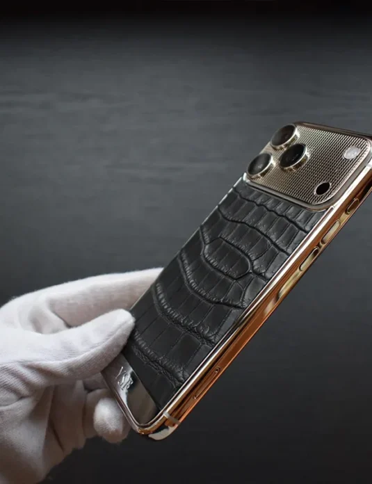Platinum crocodile iPhone 17 Pro Max with black crocodile leather back and rose gold frame held by white gloved hands